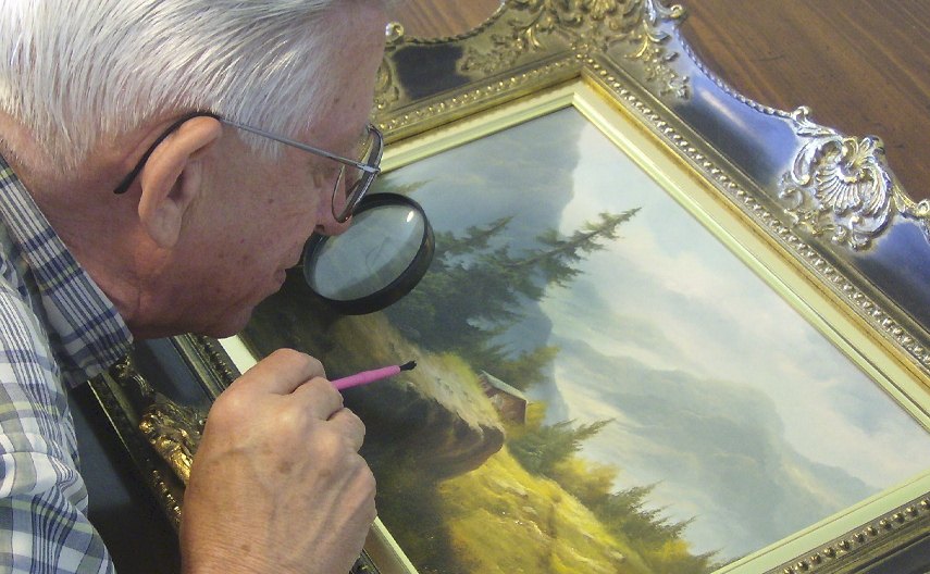 Photo of a man examining a print artwork from up close as he hopes to find an answer on how to find the value of artwork and search for more prices and sales information on the work
