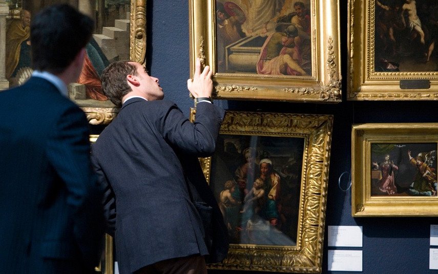 A man taking a look at the condition of a painting in search for additional information he could use to find out how to find the value of artwork