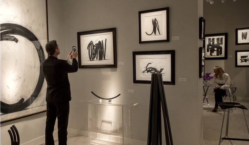 Image of a customer at art sales who photographs the piece, as buyers often do this to set the price later